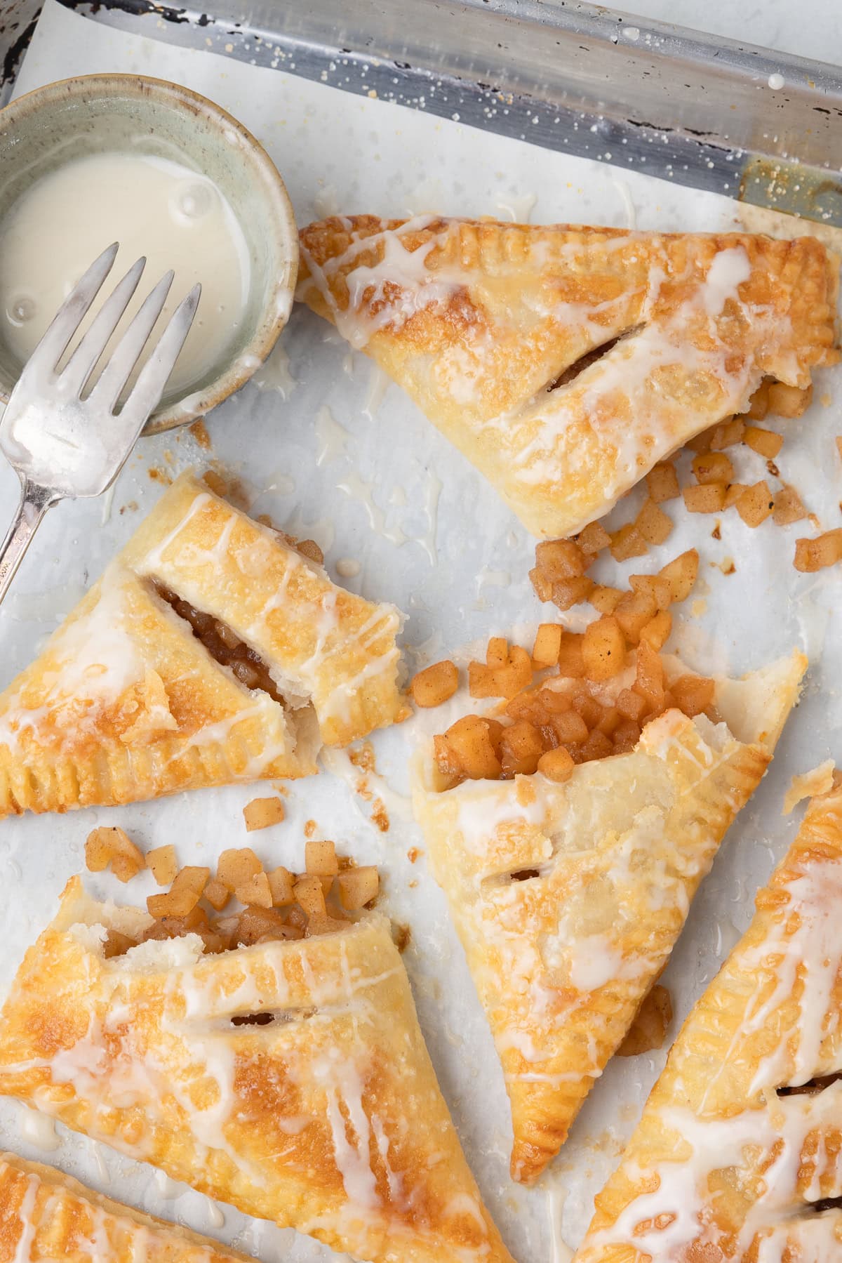 Golden baked apple turnovers drizzled with a white glaze broken open with apple filling spilling out.