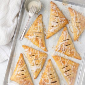 Parchment covered baking pan of golden apple turnovers in puff pastry and kitchen towel.