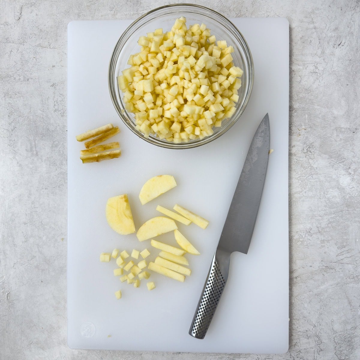 Dicing apples on a white cutting board with a chef's knife.