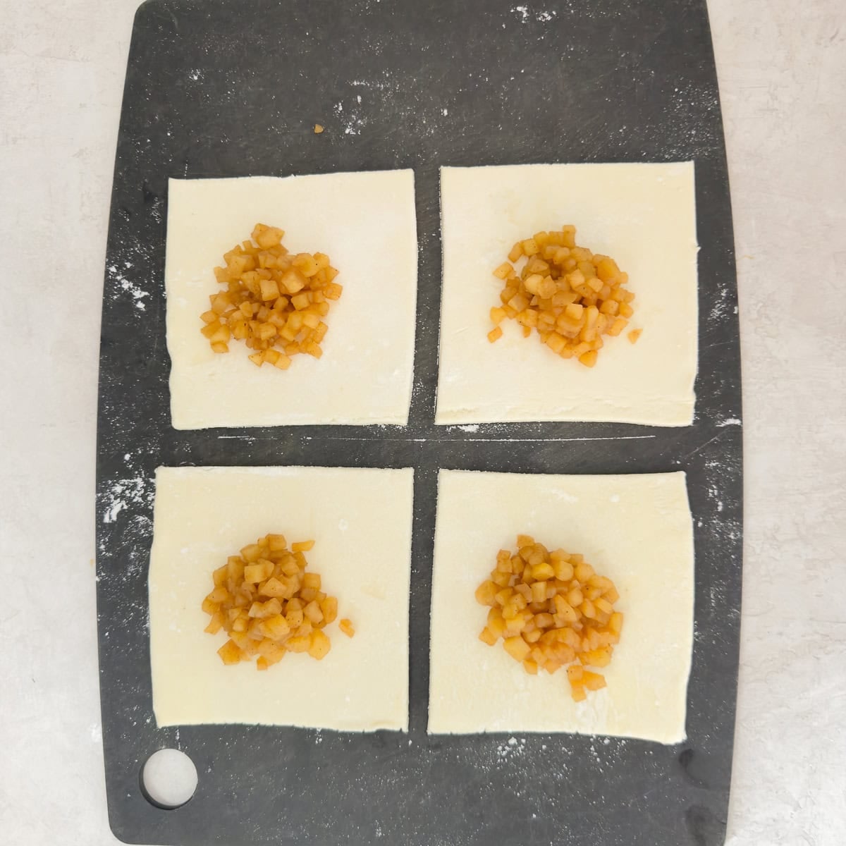 Cooked apple filling in the center of puff pastry squares for turnovers.