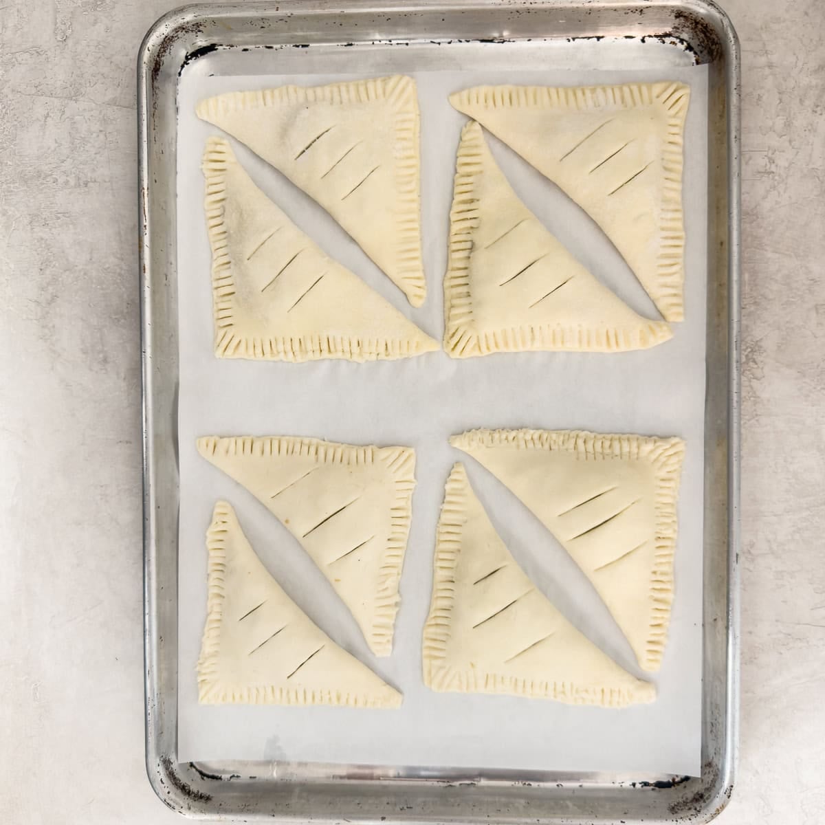 Eight puff pastry apple turnovers on a parchment lined baking sheet.