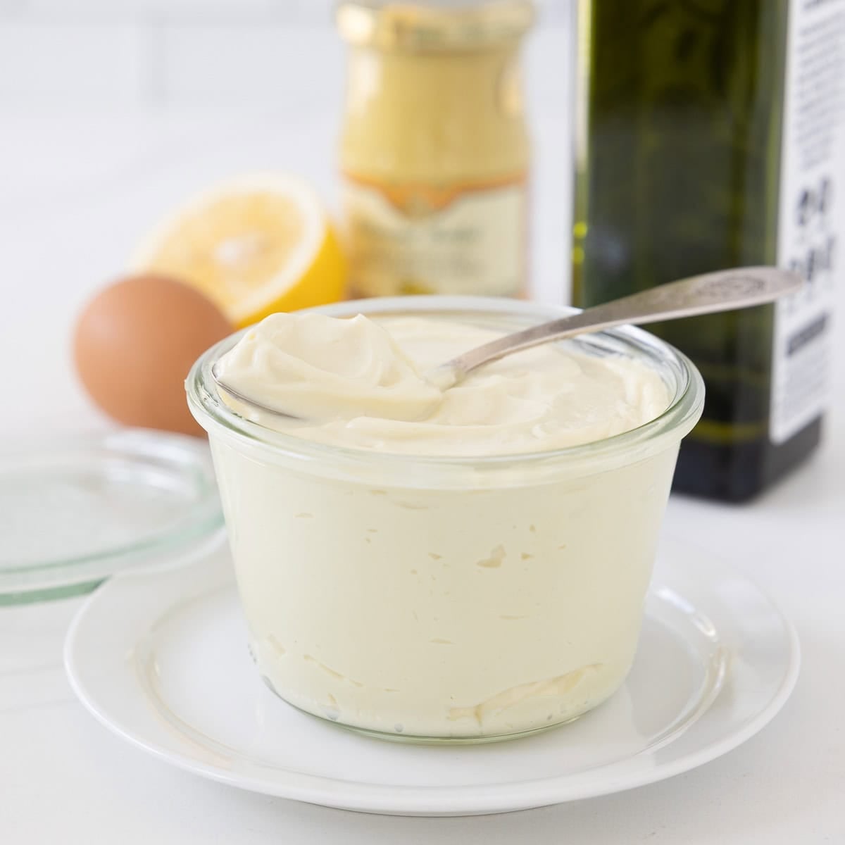 A jar of creamy avocado oil mayonnaise with a spoon on top and swirl of mayo.
