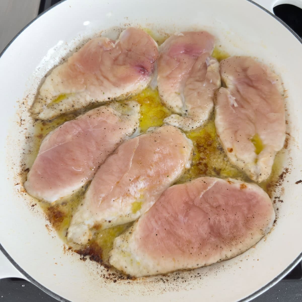 Chicken breasts browning in a wide white pan. 