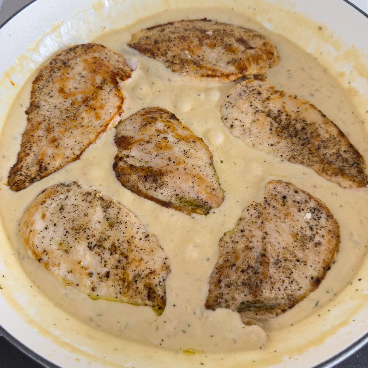 Seared boneless skinless chicken breasts in a pan with a cheesy sauce ready to serve.