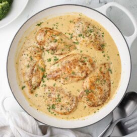 A pan of boursin chicken breasts with creamy sauce, ready for dinner with serving utensils.