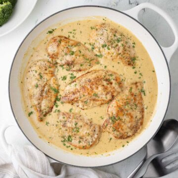 A pan of boursin chicken breasts with creamy sauce, ready for dinner with serving utensils.