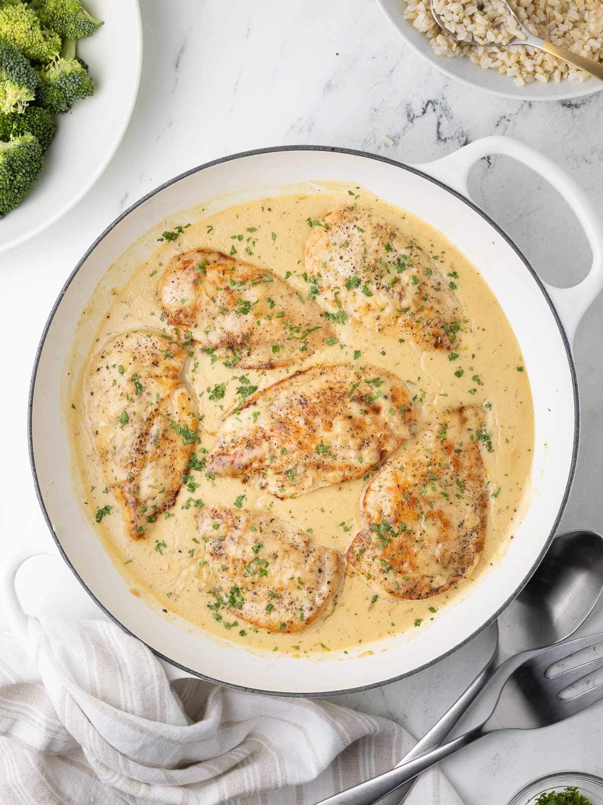 A pan of creamy golden boursin chicken breasts with creamy sauce, rice, and broccoli.