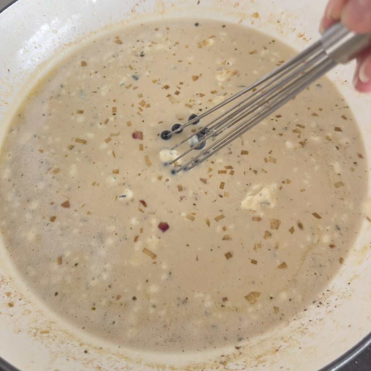Whisking a boursin cheese sauce with shallots in a wide shallow pan. 