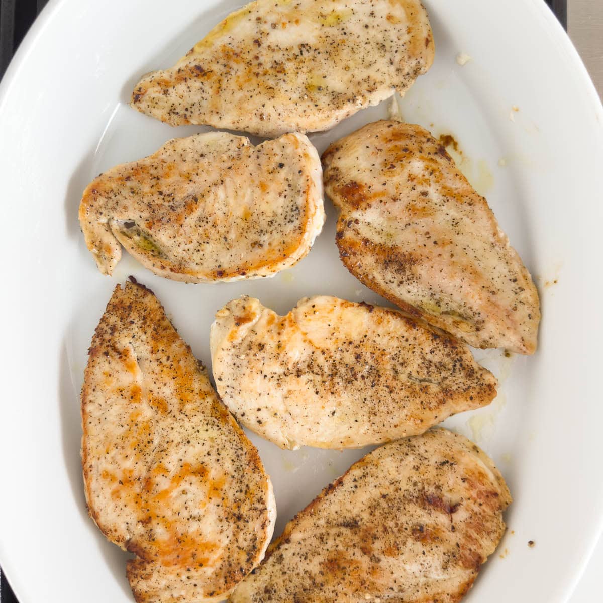 Browned boneless chicken breasts in a white casserole dish awaiting the next step.