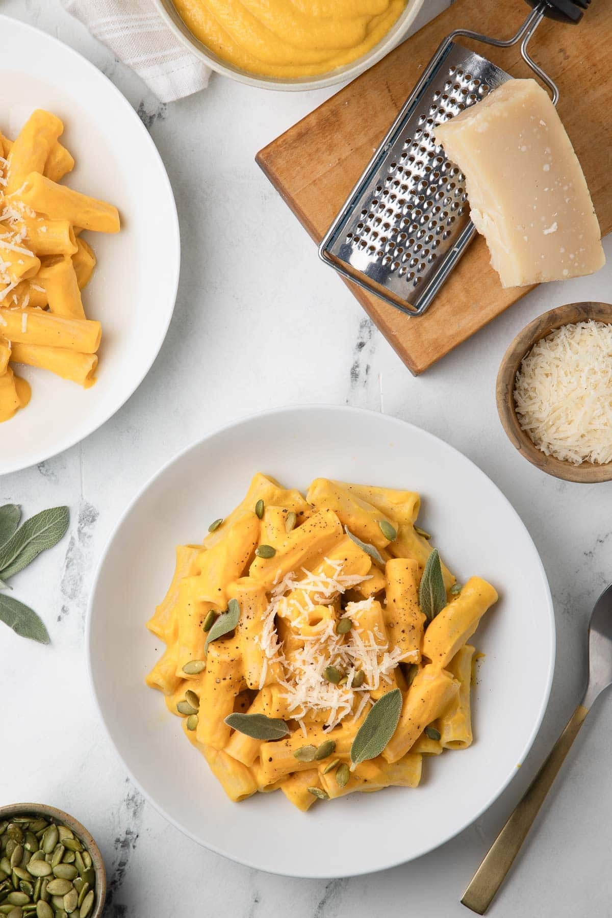 A bowl of butternut squash pasta sauce with sage leaves, parmesan cheese, and pepitas. 