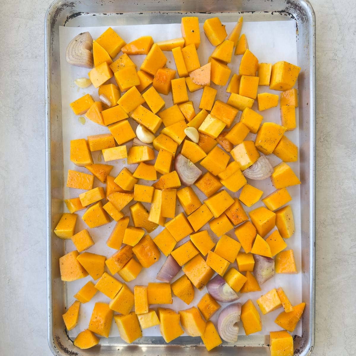 Squash and vegetables on a parchment lined baking sheet for roasting.