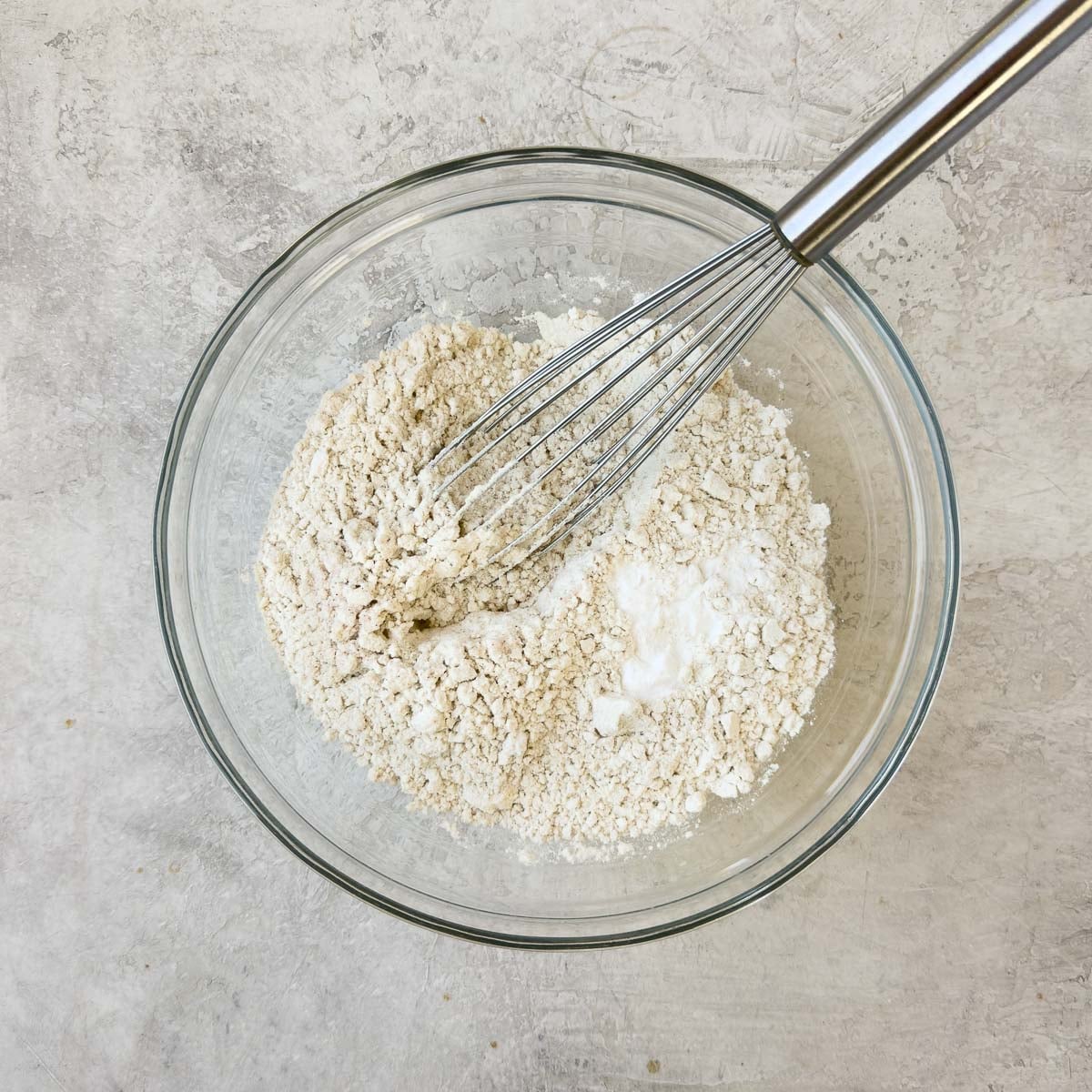 Blending flour, baking soda, and salt in a glass bowl with a silver whisk.