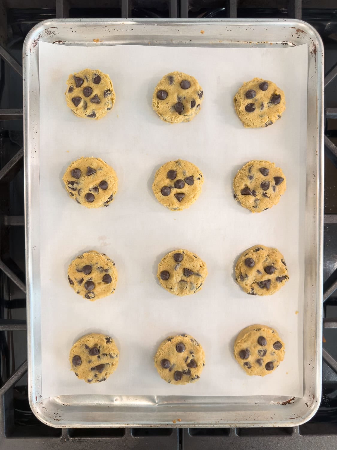Chocolate chip cookie dough portioned into cookies for baking on a baking sheet.