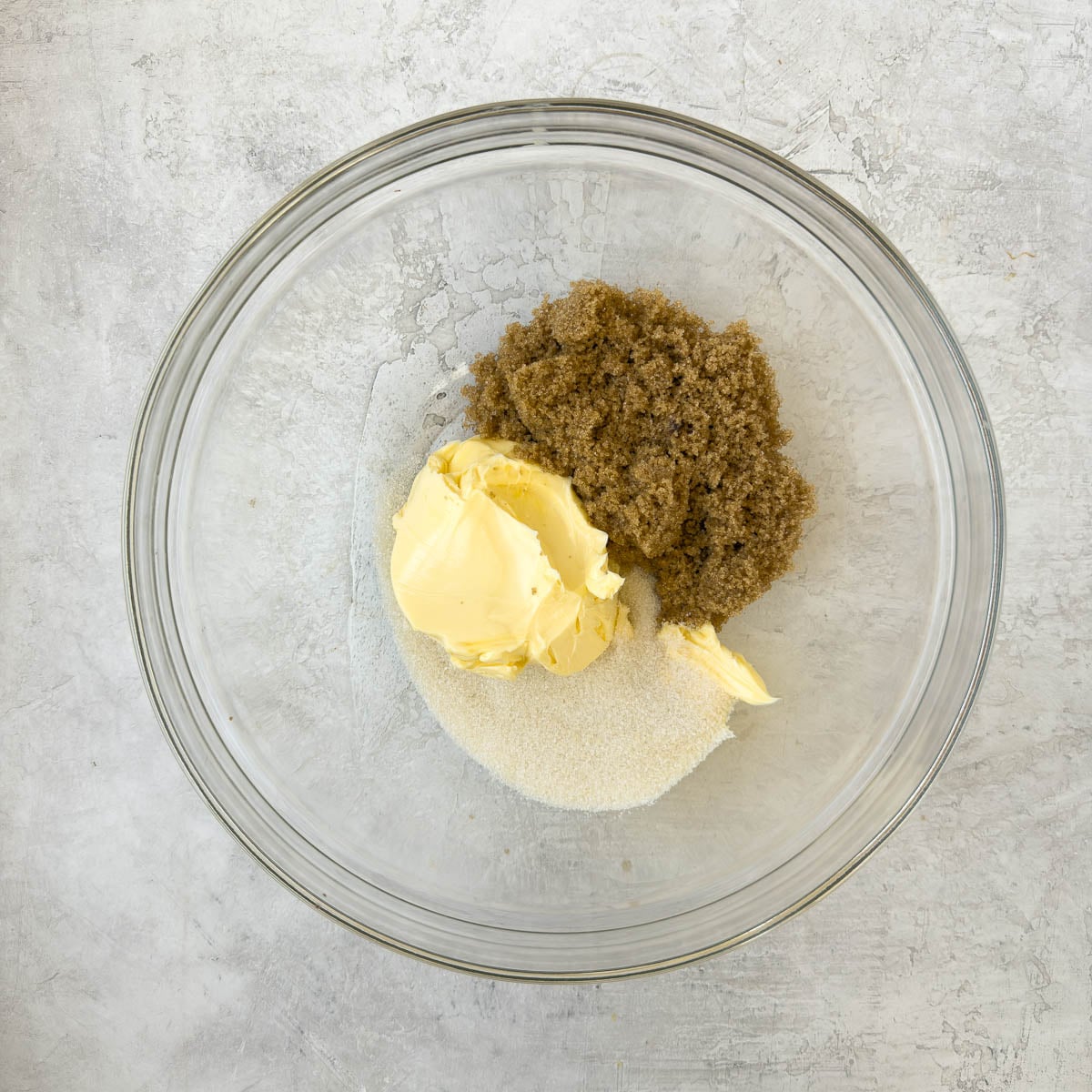 Soft butter, brown and regular sugar in a glass bowl for creaming for cookies.