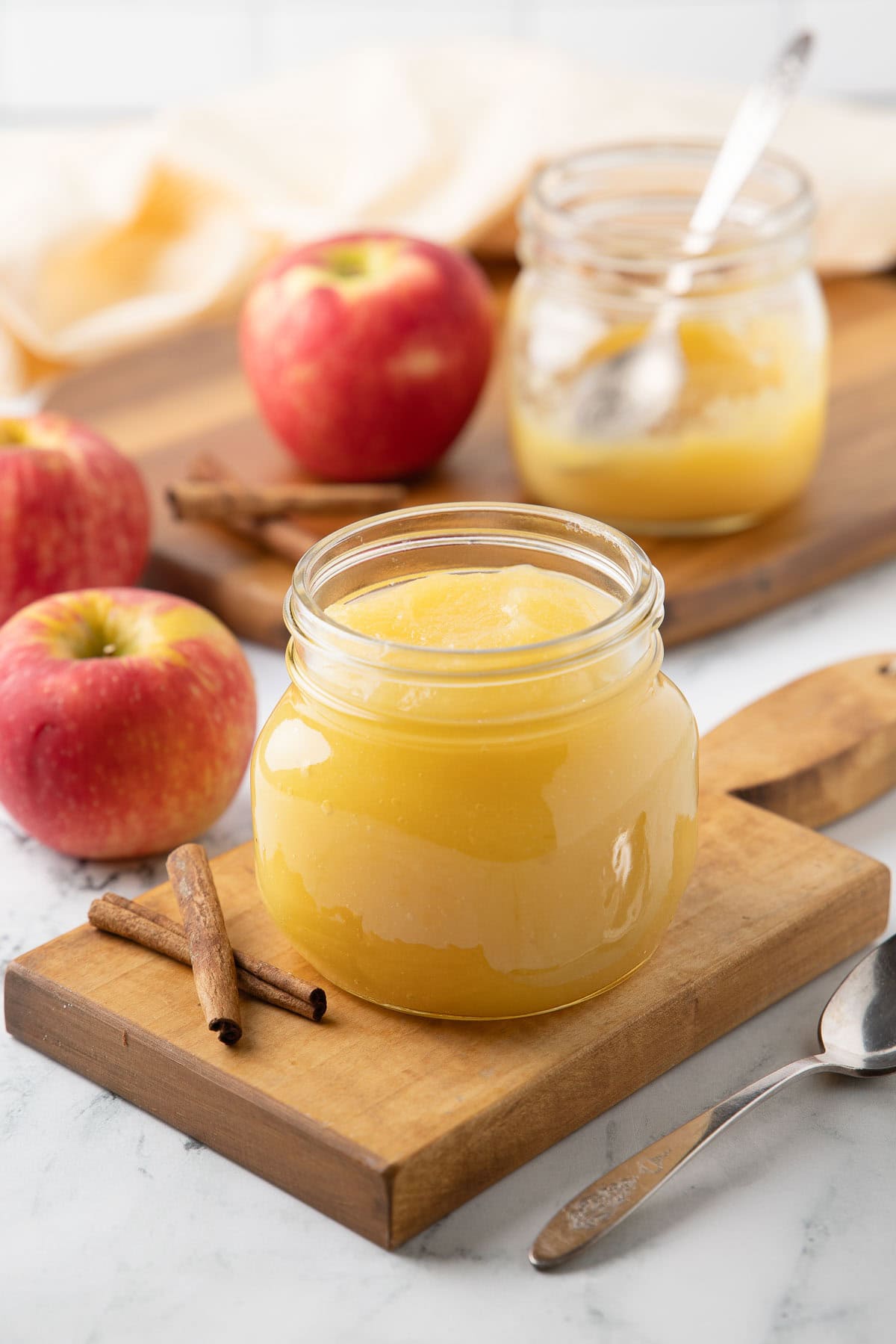 A jar of golden smooth homemade applesauce on a small wood cutting board, apples on the side.