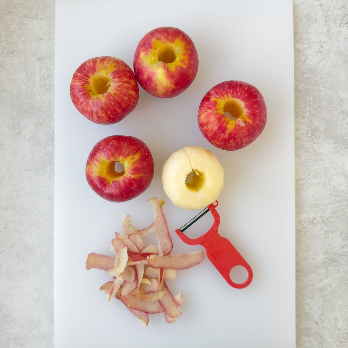 Peeling and coring apples on a white cutting board.