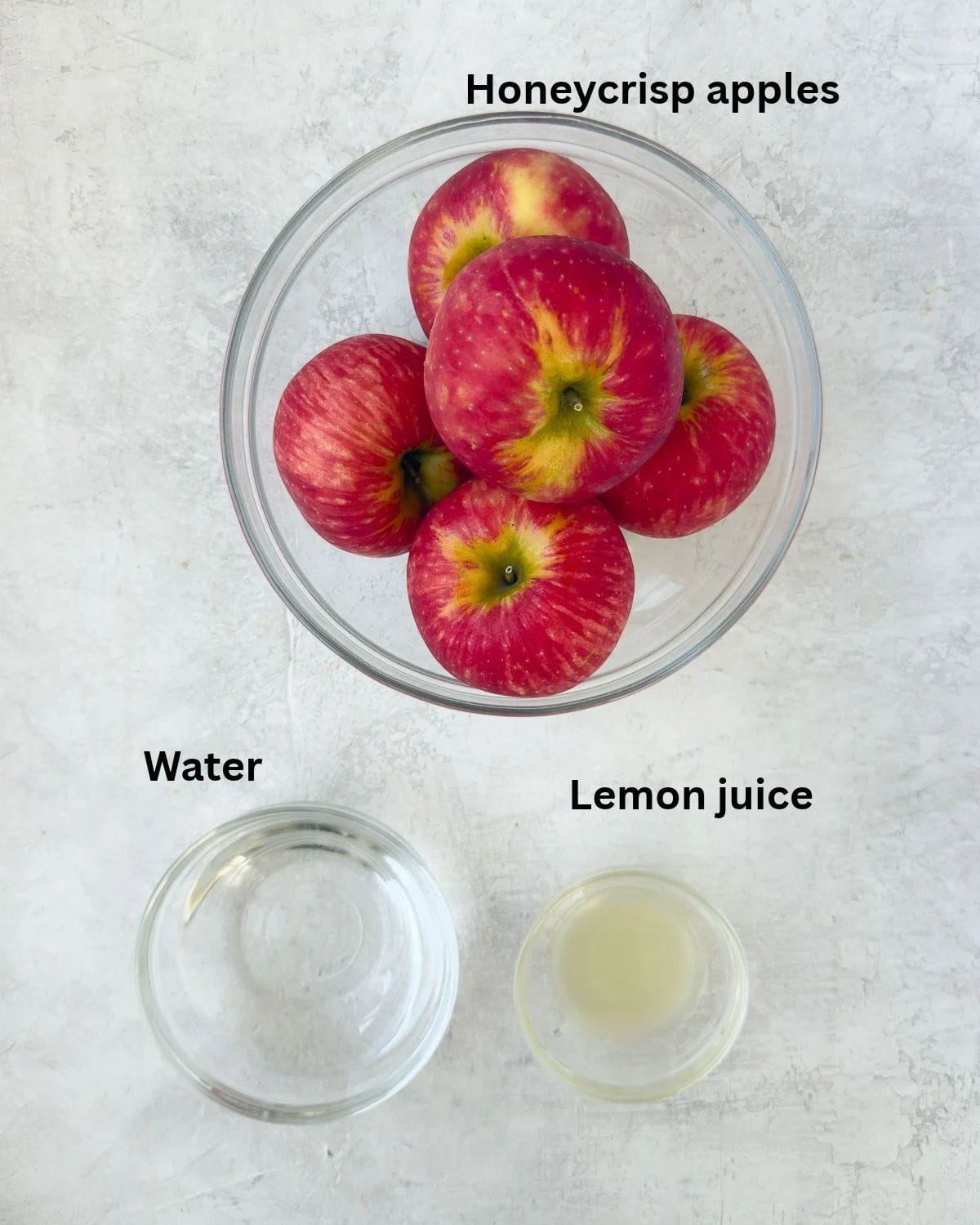 Honeycrisp apples, water, and lemon juice to make applesauce on a white cutting board.