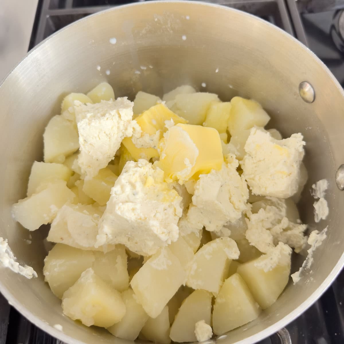 Cooked potatoes, Boursin cheese, butter and milk in a pot for whipping.