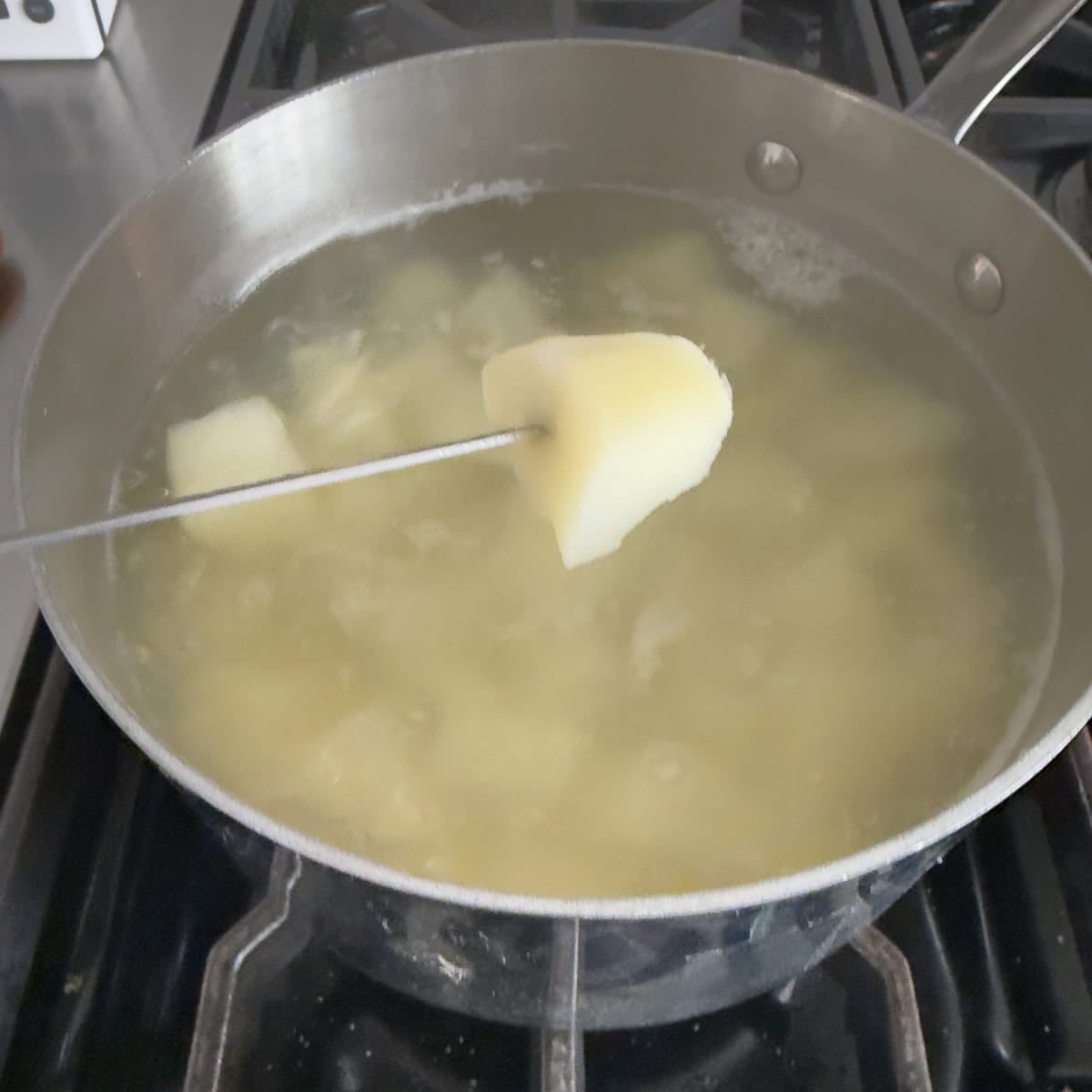 A cooked potato on the tip of a paring knife over a pot.