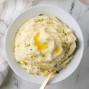 Boursin mashed potatoes with melted butter in a white bowl with gold spoon.