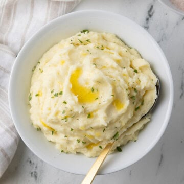 Boursin mashed potatoes with melted butter in a white bowl with gold spoon.