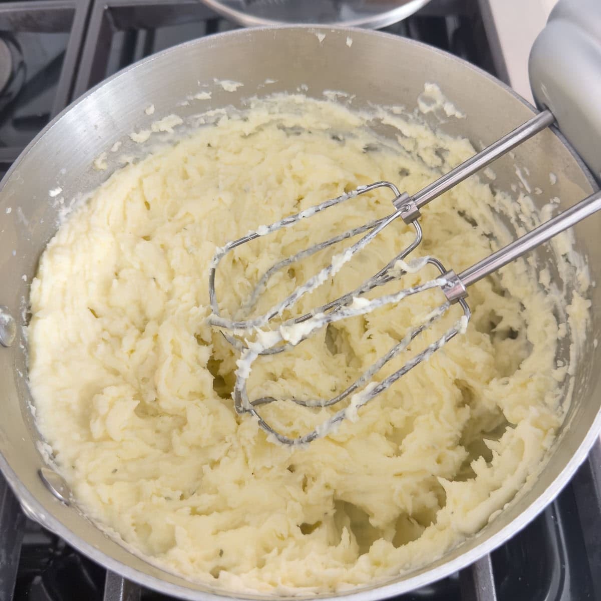 Boursin whipped potatoes with beaters in a pot on the stove.