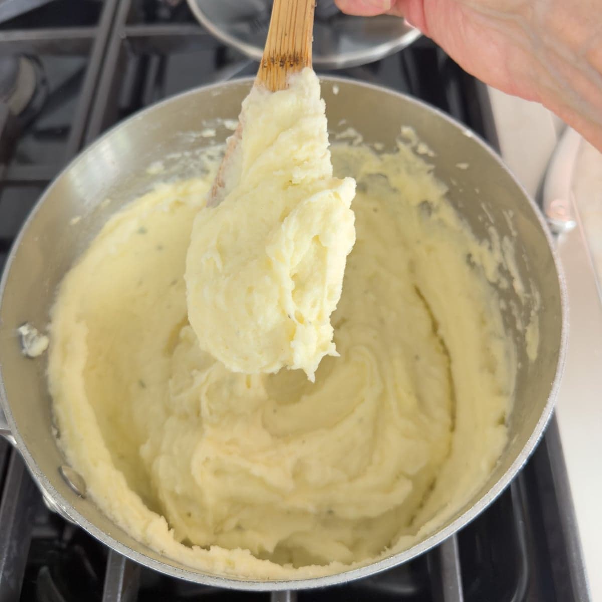 Creamy Boursin mashed potatoes on a wooden spoon over a pot.