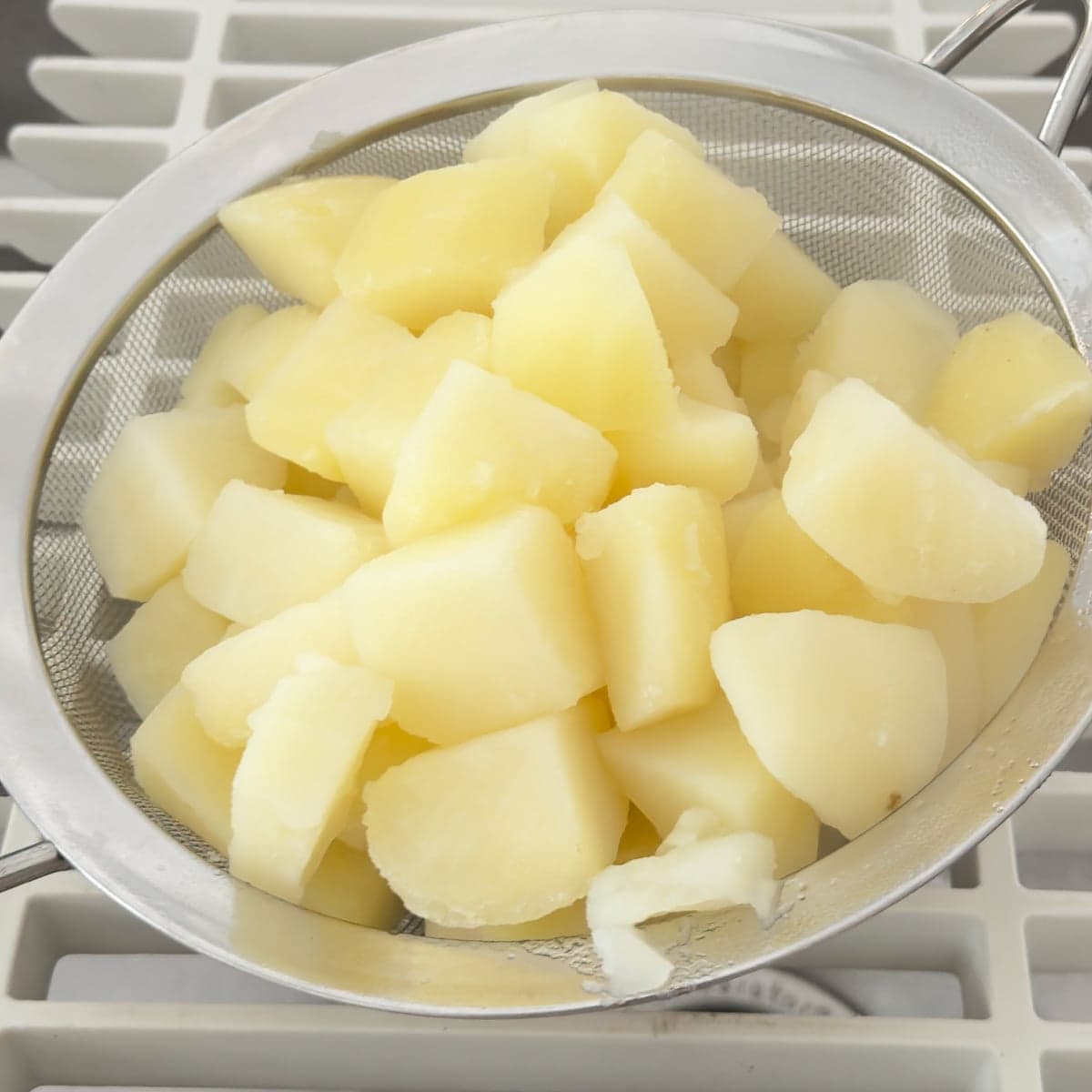 Cooked potatoes being strained over a sink.