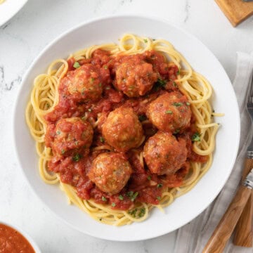 White bowl of spaghetti with ricotta meatballs and a sprinkle of parsley.