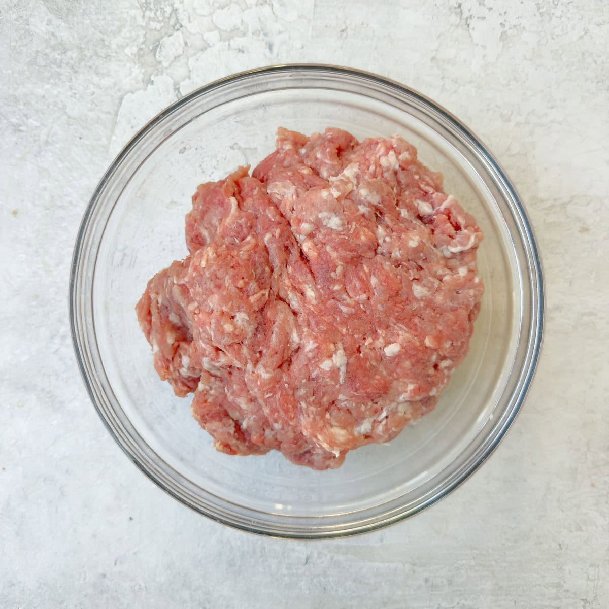 Ground pork and lean ground beef mixed together in a glass bowl for making meatballs.