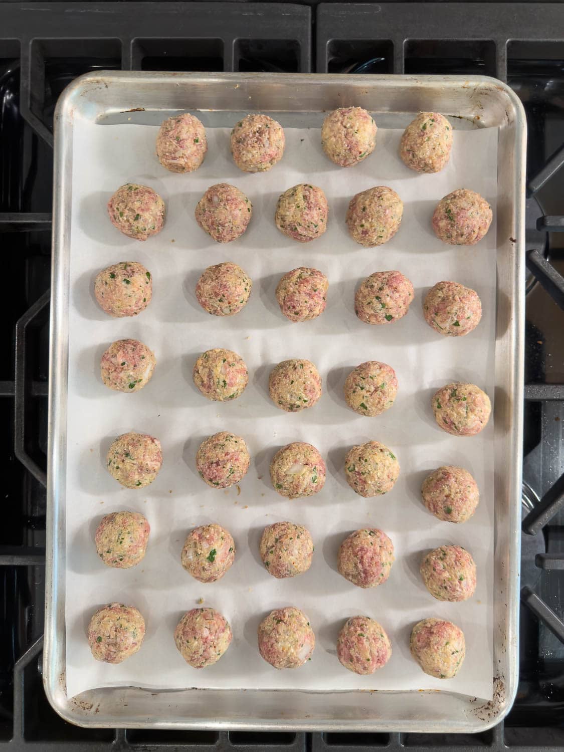 A baking sheet filled with rolled meatballs ready for baking.