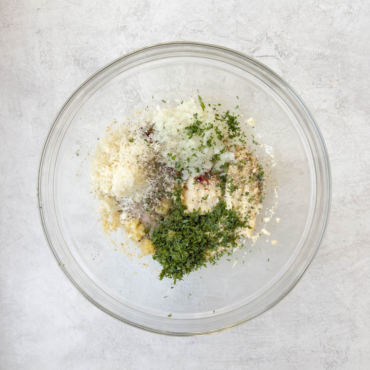 Herbs, garlic, Parmesan, onion, and seasonings added to a bowl.