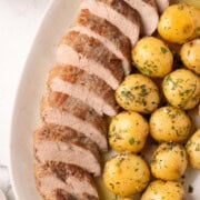 A serving plate filled with sliced over roasted pork tenderloin and gold baby potatoes with herbs.