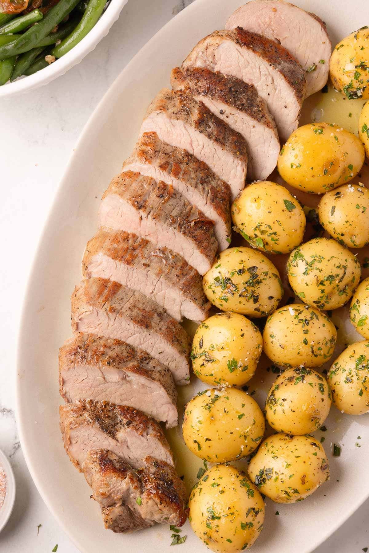 A platter of oven roasted pork tenderloin and baby gold potatoes with herbs.