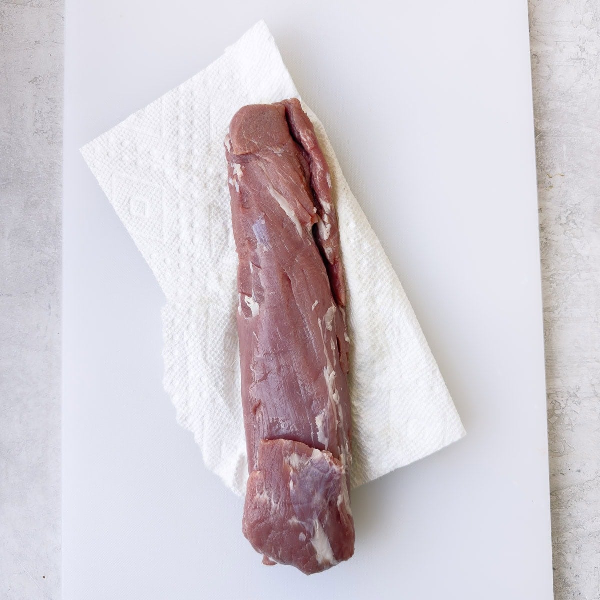 Patting a pork tenderloin dry with paper towels.