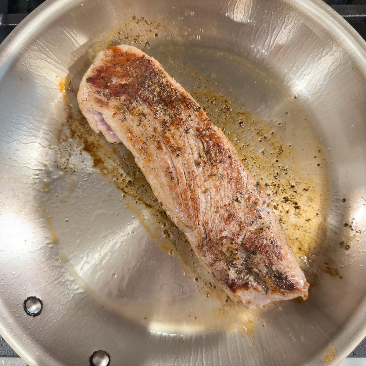 A golden brown pork tenderloin seared in a hot fry pan.