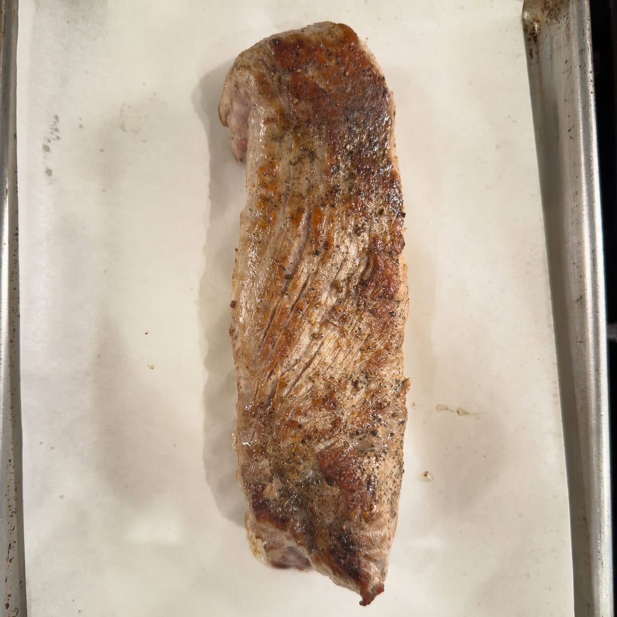 Tenderloin ready for the oven on a parchment lined rimmed baking sheet.